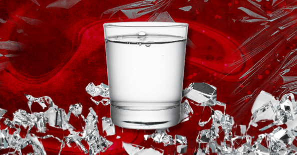 A clear glass filled with water on a red backdrop surrounded by shards of broken glass.