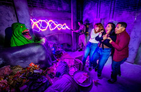 Three young adults cower in front of Slimer, a green ghost, in a Ghostbusters-themed haunted house.