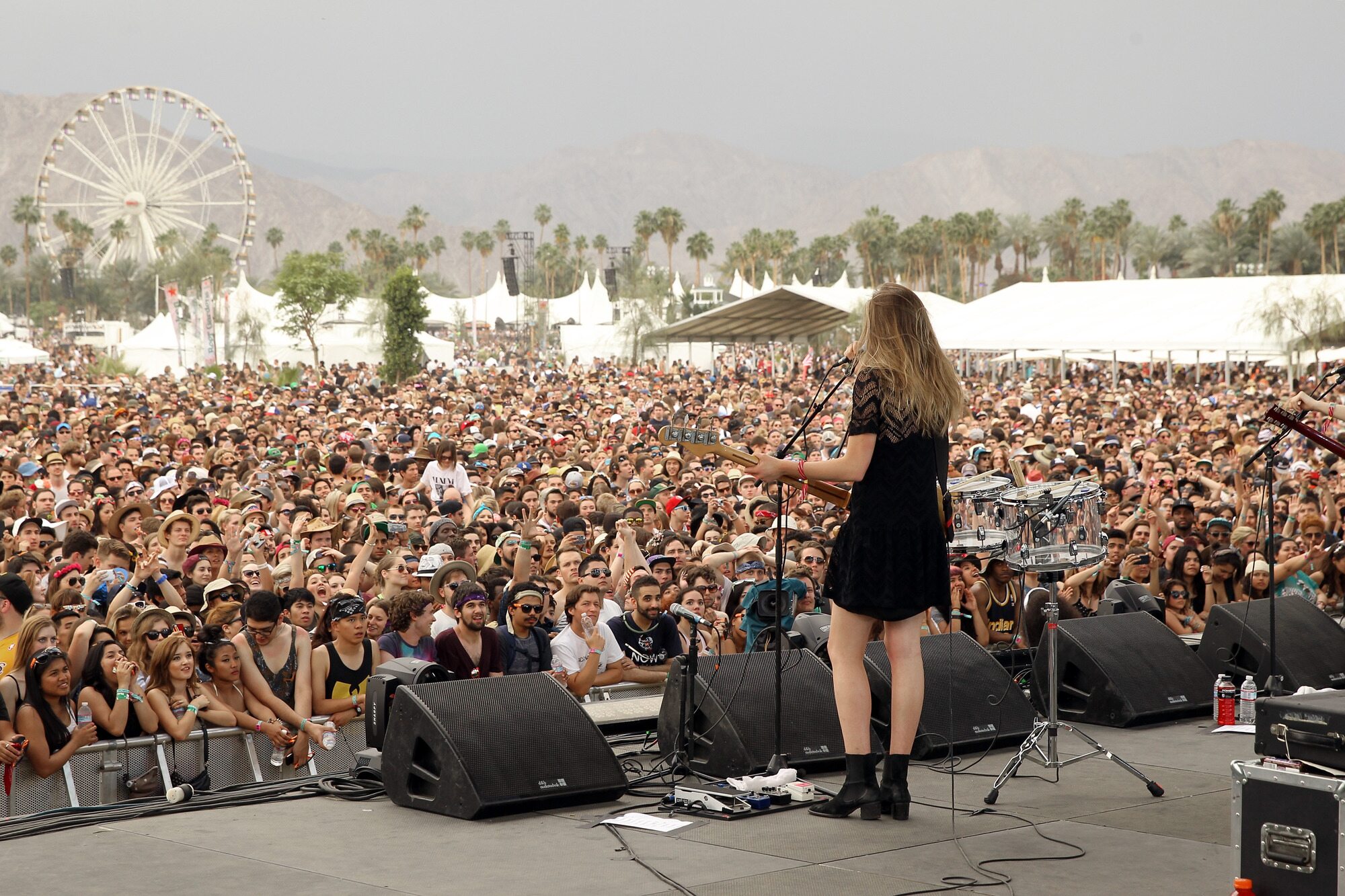 A performer on stage facing a massive crowd at the Coachella music festival with a Ferris wheel visible in the background.