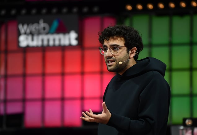 Kalshi co-founder and CEO Tarek Mansour speaking on stage at Web Summit wearing a black hoodie and headset microphone.