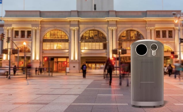 A digital rendering of the "Slim Silhouette" trash can, a sleek stainless steel bin with two circular openings, positioned in a public plaza.