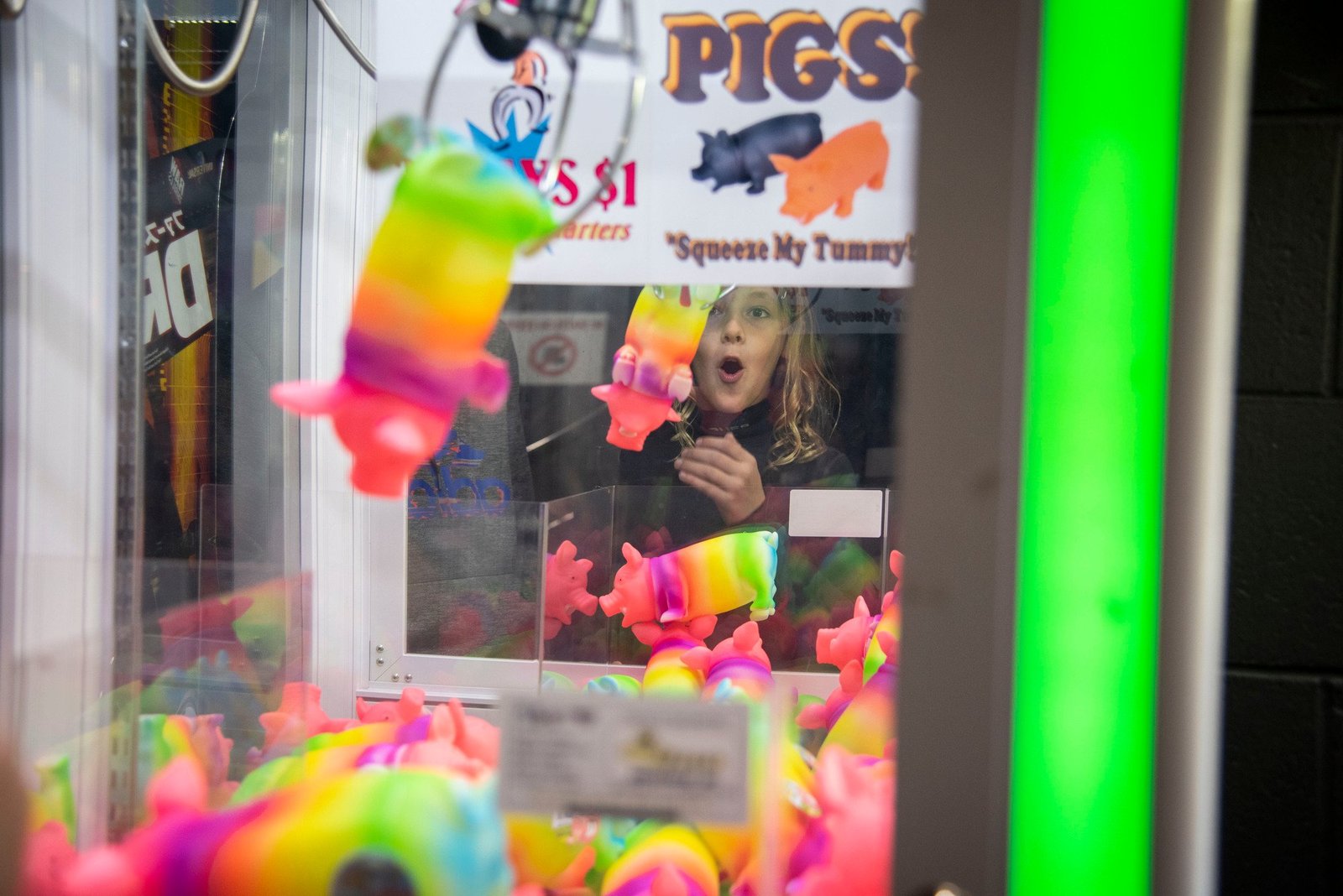 The "Almost-Win": A young girl watches with an open-mouthed, excited expression as a claw attempts to grab a rainbow-colored pig toy.
