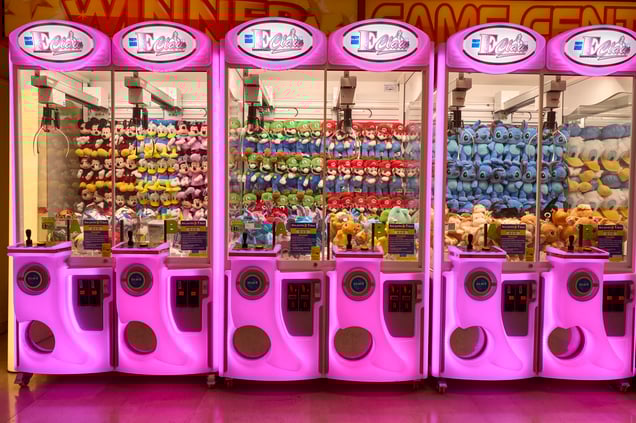 Italian Arcade: A row of pink and white claw machines in Italy filled with licensed plushies like Mickey Mouse and Mario.