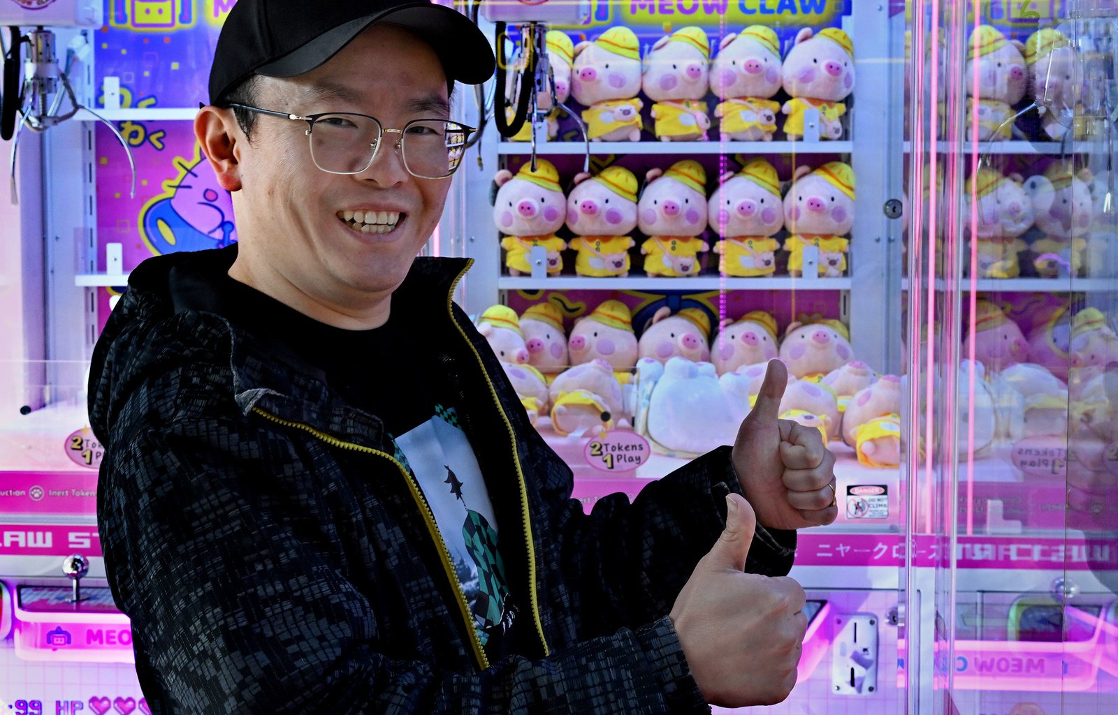 Meow Claw Arcade: A man gives two thumbs up in front of a "Meow Claw" machine filled with identical pig plushies at an arcade in Maryland.