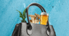 A black leather purse with a plant, mushrooms, and a glass of beer sticking out of it on a blue background.