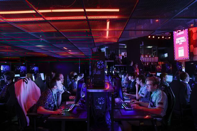A photo showing numerous competitors in a dimly lit arena, intensely focusing on their computer monitors during the semi-finals of an Excel championship.