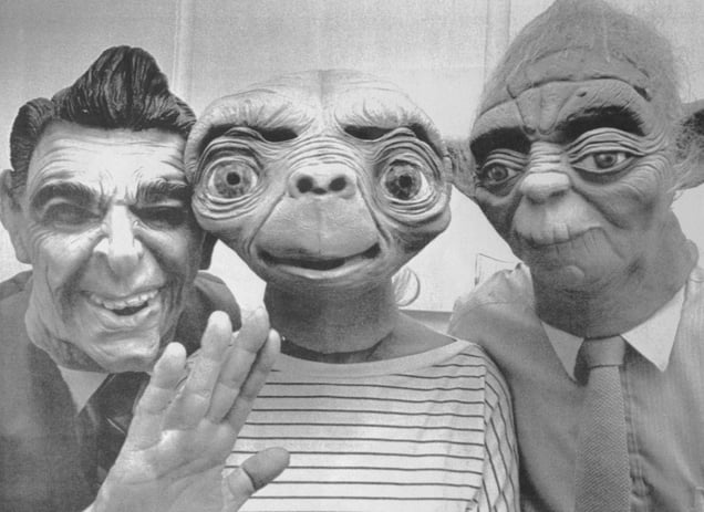 A black-and-white photo from 1982 shows masks of Ronald Reagan, E.T., and Yoda worn by people