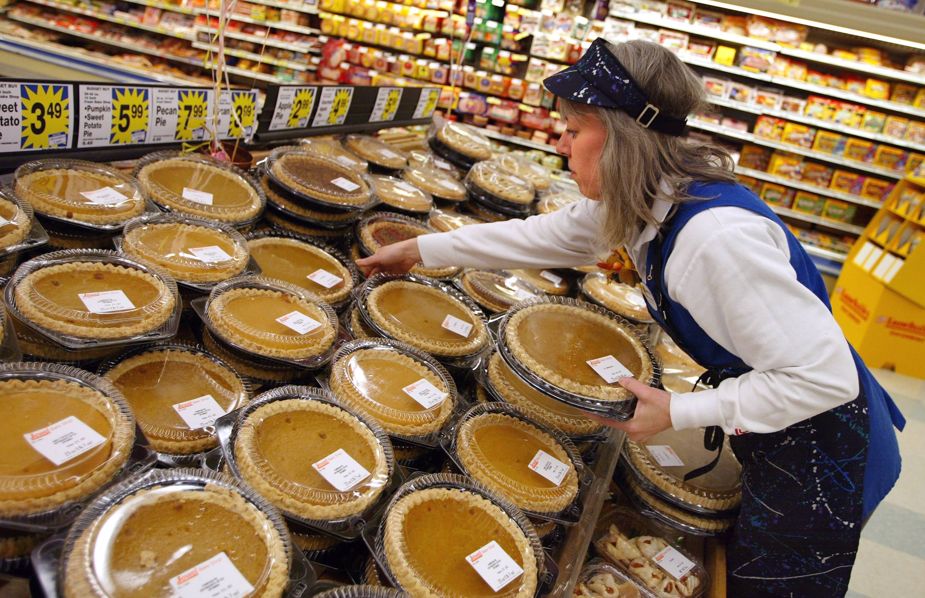 A grocery store employee arranges pumpkin pies on a display shelf.