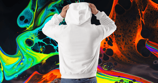 A man wearing jeans and a white hoodie with the hood pulled up stands facing away from the camera. 