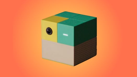 A Nex, a square gaming console with a beige bottom and yellow and teal top.