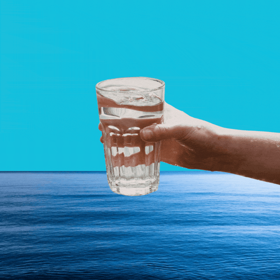 A glass of water being dipped into the ocean.