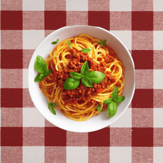 A plate of spaghetti on a red-checkered tablecloth with an ear emerging from either side.