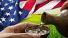 Two hands for sake into a cup in front of a green field and an American flag. 