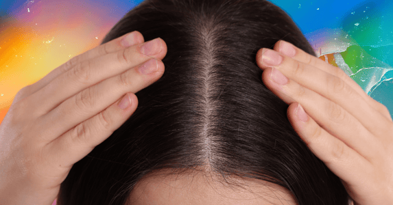 A woman parts her brunette hair revealing her scalp. 