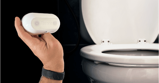 A rounded white device is held up in front of a toilet.