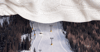 A white knit blanket covers the top third of a photo of a ski slope. 
