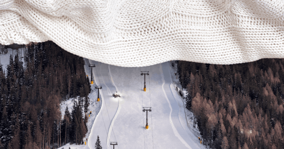 A white knit blanket covers the top third of a photo of a ski slope.