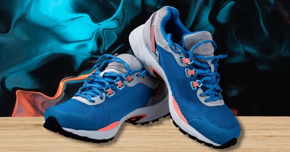 Blue running sneakers with gray and orange trim on a black, orange, and blue wavy background.