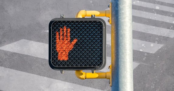 A crosswalk sign with the red hand showing and a crosswalk in the background.