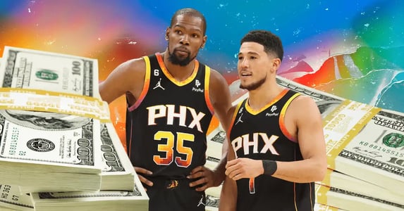 Basketball players Kevin Durant and Devin Booker wear black Phoenix Suns uniforms with stacks of $100 bills surrounding them.
