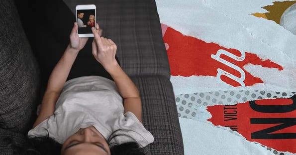 A white woman with dark hair in a white T-shirt laying back on a couch and watching a woman slap a man on her cell phone.