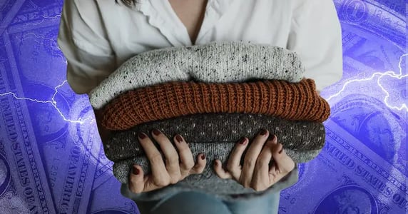 A person holds a stack of folded sweaters in their hands.