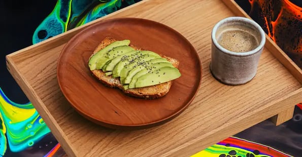 A plate of avocado toast sits on a wooden tray against a colorful background.