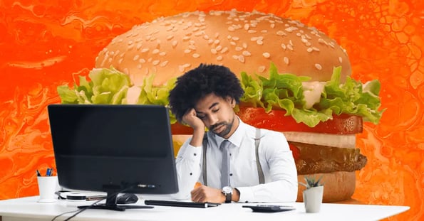 A Black man in suspenders, a tie, and a white dress shirt leaning on one arm and falling asleep at a desk in front of a computer, with a large hamburger in the backdrop.