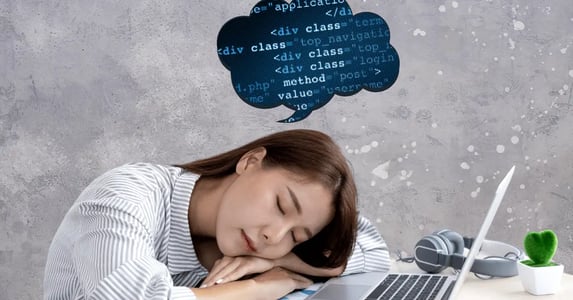 An Asian woman sleeping at her desk with a laptop and headphones. A thought bubble filled with computer code hovers over her head.
