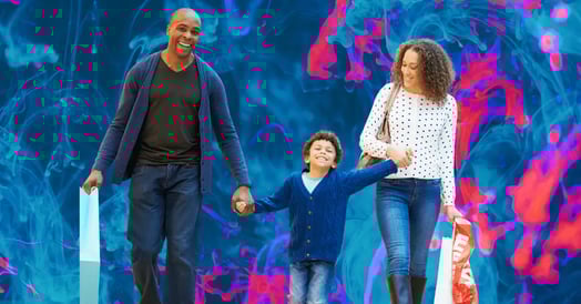 A Black man, woman, and little boy smiling and walking, holding shopping bags.