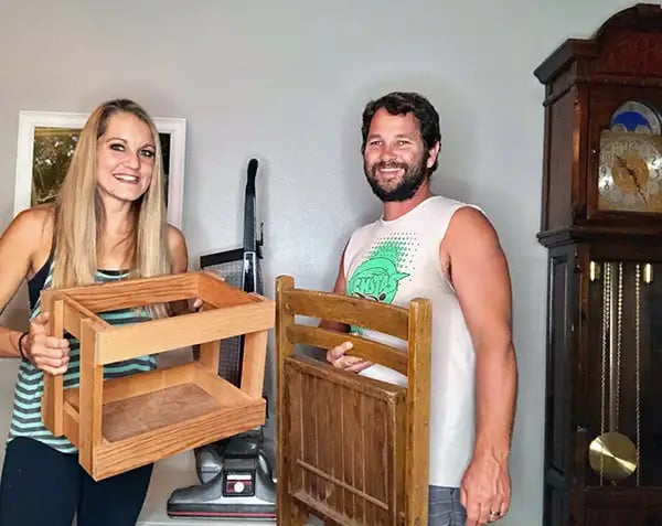 Rob holding a chair and Melissa holding a crate in 2019