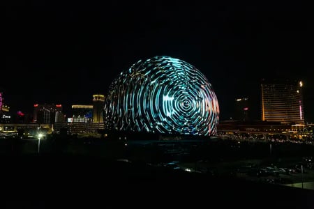 A giant sphere displaying a blue swirl pattern lights up a Las Vegas street at night.