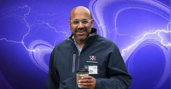 Niraj Shah holding a cup of coffee on a purple background.