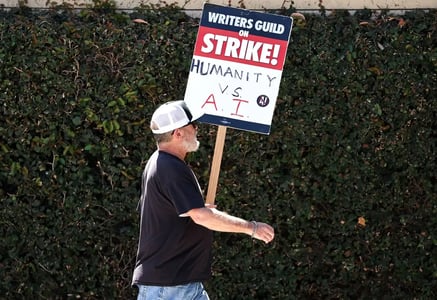 A man carries a WGA (Writers Guild of America) sign that reads 'Humanity vs. AI.'