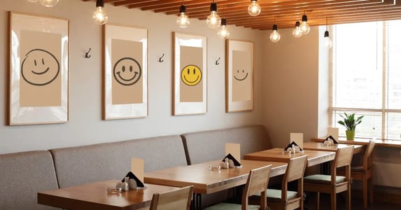 A restaurant dining room with four picture frames of smiley faces over four dining tables.