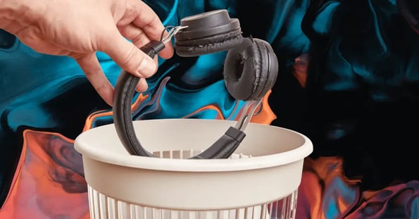 A pair of headphones is dropped into a waste bin.