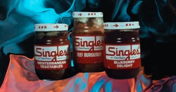 Three Gerber Singles glass jars labeled “Mediterranean vegetables,” “beef burgundy,” and “blueberry delight” on a blue and orange background.