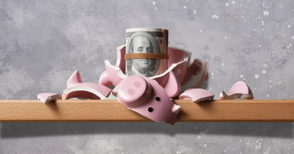 A pink piggy bank smashed to pieces on a wooden shelf, revealing a roll of cash.