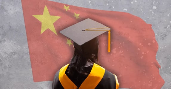 The back of a woman’s head who has black hair and is wearing a graduation cap and gown with China’s flag in the background.