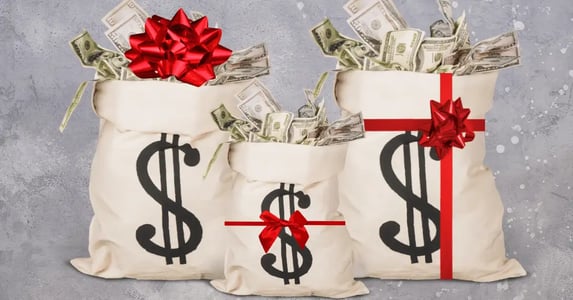 Three beige sacks with dollar signs on the front filled with cash and wrapped in a red gift bow.