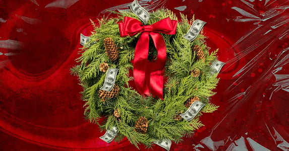 A Christmas wreath made out of pine branches, pine cones, and dollar bills with a red bow on a red background.