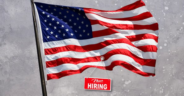 An American flag with a red “Now hiring” sign hanging from it.