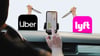 A driver touches a map on their phone. Uber and Lyft app icons are shown on the dashboard with knife-wielding hands coming out of them.