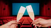 Two hands clink flutes of champagne in a movie theater.