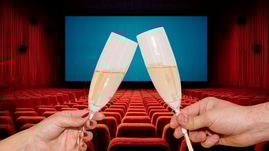 Two hands clink flutes of champagne in a movie theater.