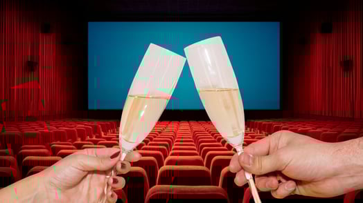 Two hands clink flutes of champagne in a movie theater.