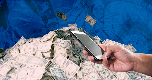 A hand holds a phone in front of a pile of cash against a blue background.