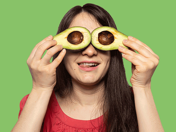 Woman holding a halved avocado over her eyes