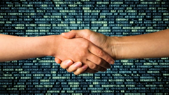 Two people shake hands. In the background is computer code.