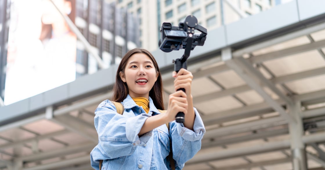 A young Asian woman in a blue shirt records herself with a camera.